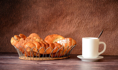 An assortment of homemade pastries in a wicker basket and a cup of hot tea on a wooden table.
