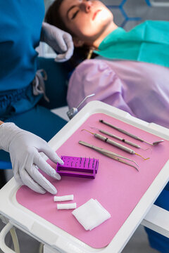 Dentist picking up instruments on a pink table next to a patient 