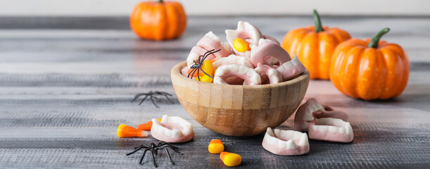 Bowl with tasty candies for Halloween on grey wooden background