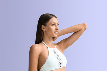 Young tanned woman in swimsuit on lilac background