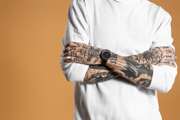 Young tattooed man in white sweater on brown background
