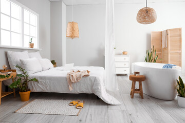 Interior of light bedroom with bathtub and houseplants