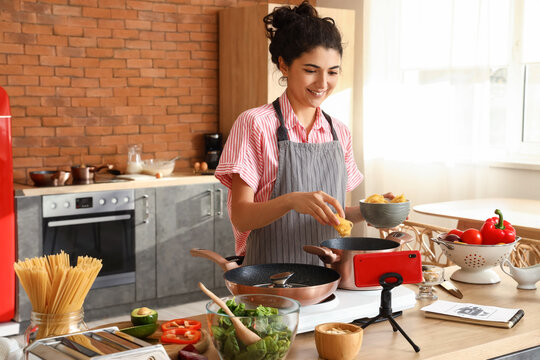 Young woman cooking pasta while watching video tutorial in kitchen
