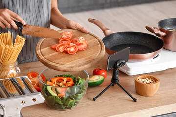 Young woman cutting tomato while following video tutorial in kitchen, closeup