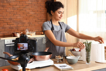 Young woman taking paper towel while recording video class in kitchen