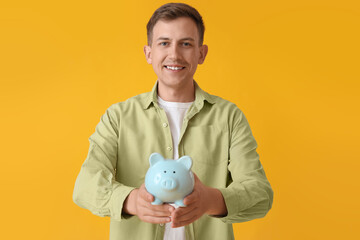Fototapeta na wymiar Young man with blue piggy bank on yellow background