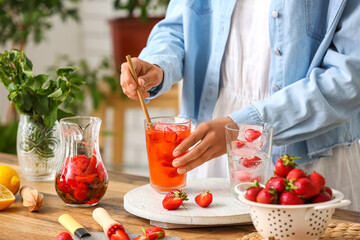 Woman with glass of cold strawberry lemonade in kitchen