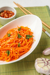 Bowl with delicious carrot salad and ingredients on green mat, closeup