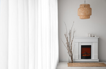 Fototapeta premium Vase with tree branches, fireplace and hanging lamp near light curtain in living room