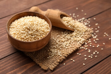 Bowl and scoop of sesame seeds on wooden background