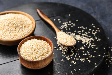 Dark wooden board with bowls and spoon of sesame seeds, closeup