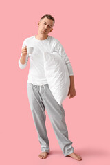 Sleepy young man with cup of coffee and pillow on pink background