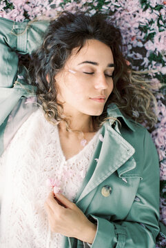 woman with closed eyes lying on the grass covered with sakura petals