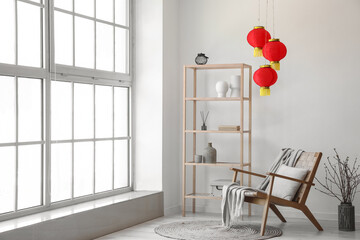 Interior of light living room with shelving unit, armchair and Chinese lanterns