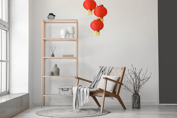 Interior of light living room with shelving unit, armchair and Chinese lanterns