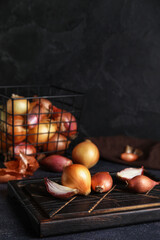Wooden board with onion on dark background, closeup