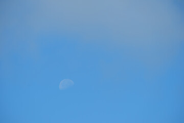The daytime moon in the blue sky is covered with a light haze.