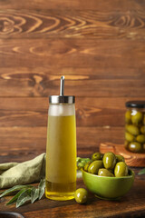 Bottle of fresh oil and bowl with olives on wooden background