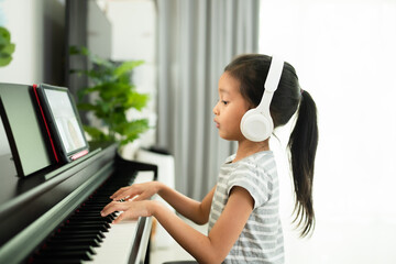 Cute asian 6 years old is enjoy playing piano of online class at home, concept of learning, art, steam, musical, mental health, homeschool, virtual, online and distance education concept.