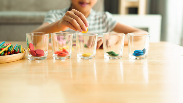 Unidentified kindergarten girl is learning to sorting the color coins to the glass, concept of homeschool, montessori, freedom, education, activity for child development and sensory activity for kid.