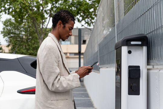 Man using smartphone to pay at recharging station 