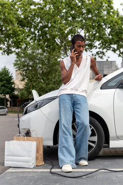 Black man talking on Smartphone While Recharging Electric Vehicle