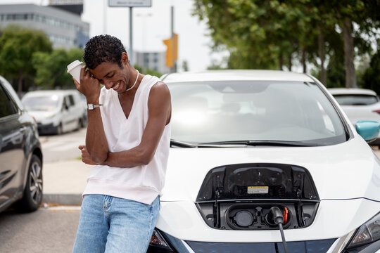 Black man having a coffee While Recharging Electric Vehicle