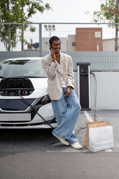 Black man talking on Smartphone While Recharging Electric Vehicle