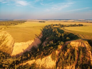 High hills with fields of grass and groves of birches. Erosion of clay hills. The light of the evening sun illuminates the clouds and the grass and trees