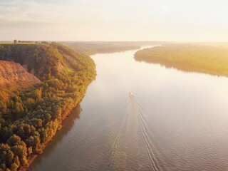 River valley with a steep bank with a forest of trees, sunlight and a boat on the water