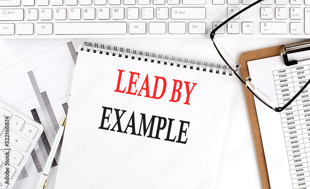 Poster text lead by example on office desk table with keyboard, notepad and analysis chart on white backgro