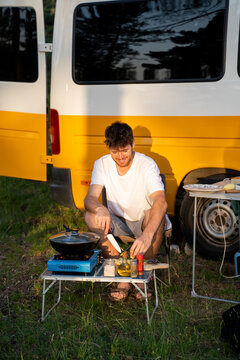Man camping and cooking with camper van in nature