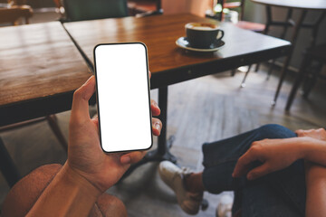 Mockup image of a man holding black mobile phone with blank white screen in cafe