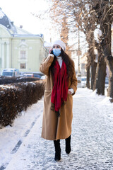a young and beautiful girl with long curly hair in a stylish coat and with a mask on her face. Living in quarantine