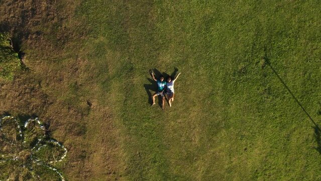 Two Happy Young People Lying On Grassy Field In Liloan, Southern Leyte, Philippines. - Drone Flying Upward