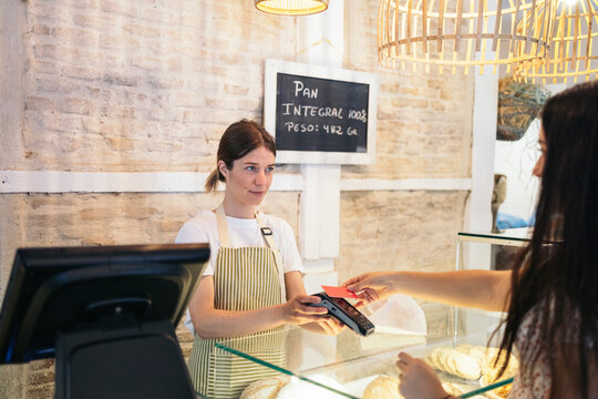 Worker of a pastry shop charging a client with the dataphone