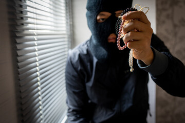 Burglar holding jewelry indoor, robbery concept.