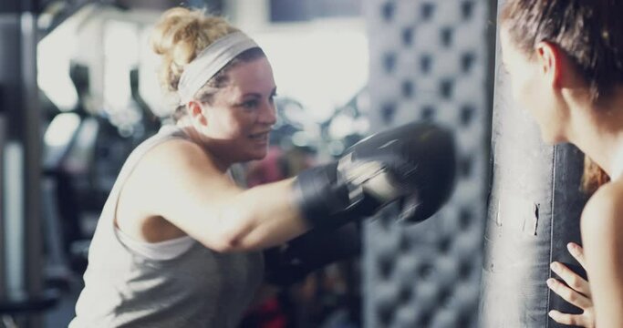 Chubby, overweight and active woman boxing during an intense workout at the gym with her fitness trainer. Sweaty, active and dedicated female wearing sports gloves while exercising for weightloss