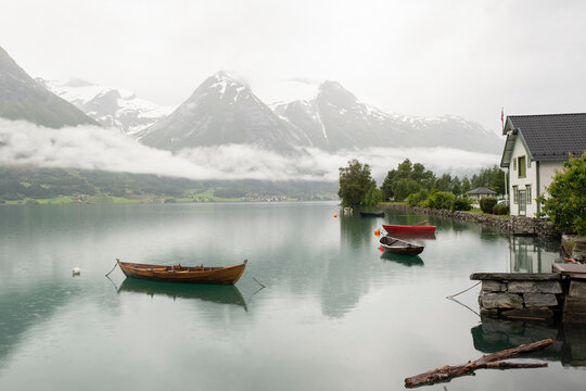 A bucolic image with moored wooden boats, a dock, o house and mountain