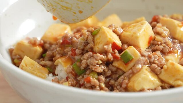 Pouring stir-fried mapo tofu with hot spicy sauce over white rice in a bowl at home