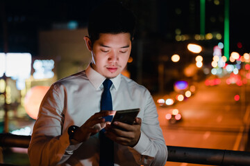 Asian businessman use mobile phone, smart phone after work walking through city street in the city at night