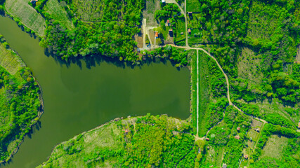 Aerial view over woodland and plots with cottages near water, lake