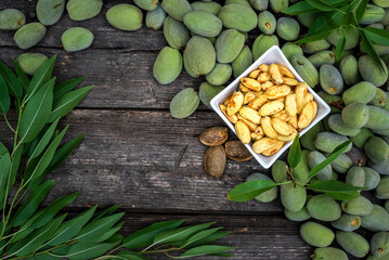 Green almonds open background   fresh raw unripe wooden rustic table blurred garden background leaves, Top view copy space shell  tree branch frame Peeled almond kernel milk husks white Bowl