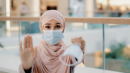 Young woman in medical protective mask shows with palm stop sign gesture forbidding to approach due...