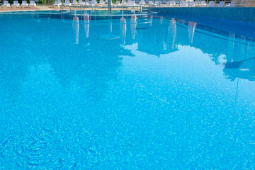 Pool side. Empty outdoors swimming pool on summer sunny day. Seaside vacation and hotel resort concept. Reflection in blue clean sea water pool