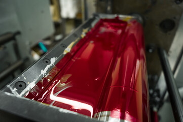 Magenta ink in the paint system compartment of a modern flexographic printing press in a print shop. Red paint in the ink feeder on the printing cylinder. Selective focus