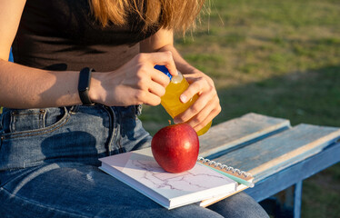 a schoolgirl girl, a high school student holding books and a red apple and juice in her hands. the concept of returning to school. outdoor activities.