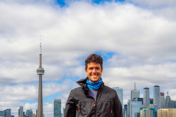A young adult man smiles to the camera with a skyscraper in his background.