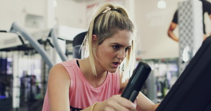 Dedicated, fit and active woman at the gym, cycling on an exercise spin bike. Focused and sporty woman working out on an elliptical machine to boost stamina and endurance at a fitness facility