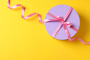 Round gift box with bow on yellow background